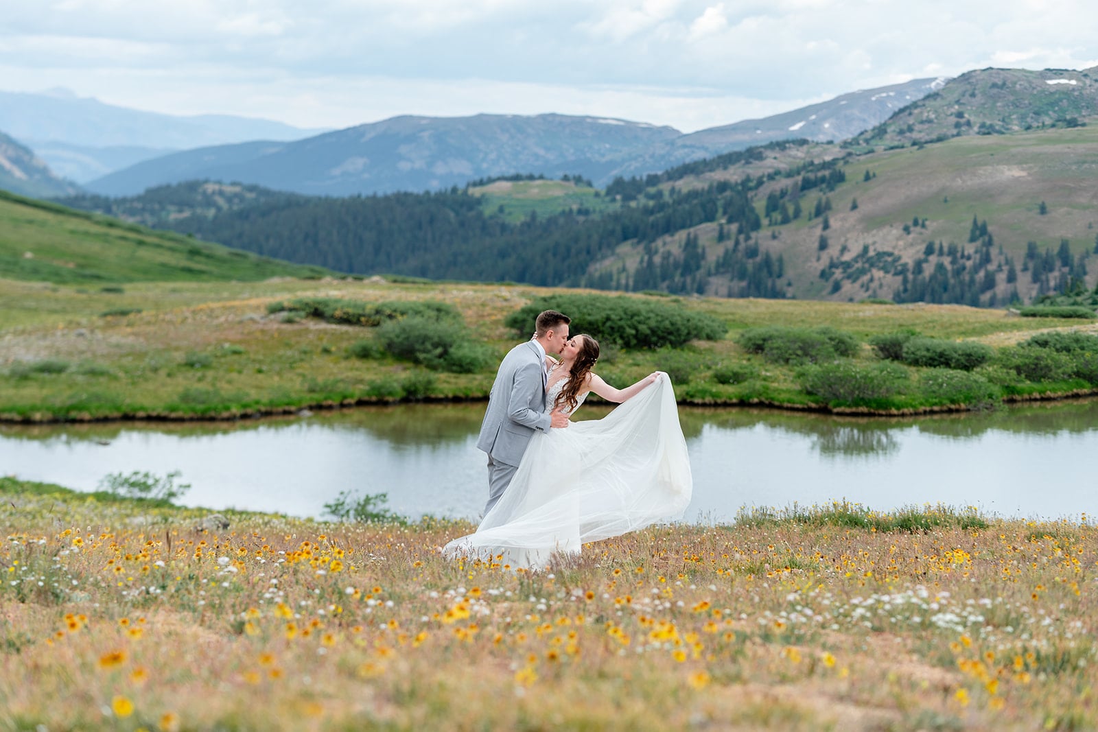 Micro-wedding ceremony beside an alpine lake in Colorado - couple exchange kiss in wildflower meadow 