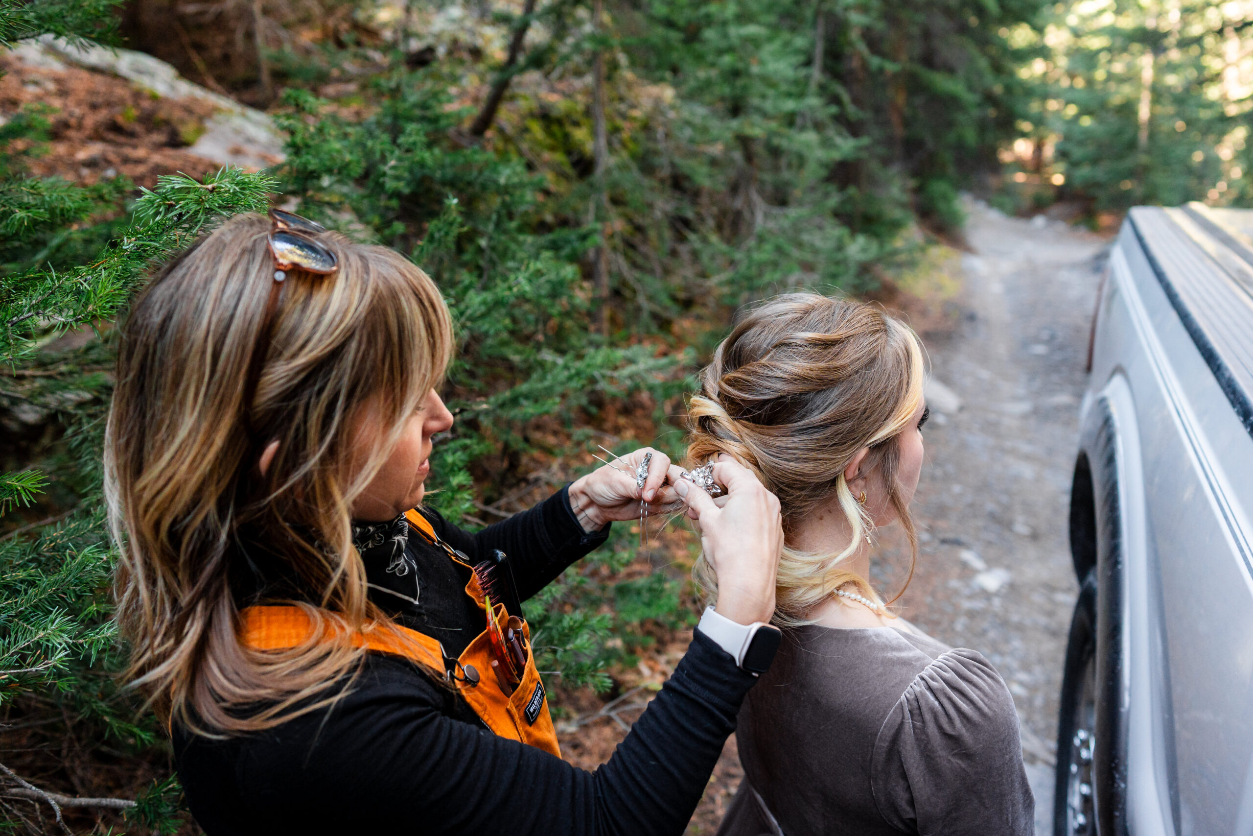 Wedding Team A hairstylist adjusting a bride's hair outdoors in a wooded area