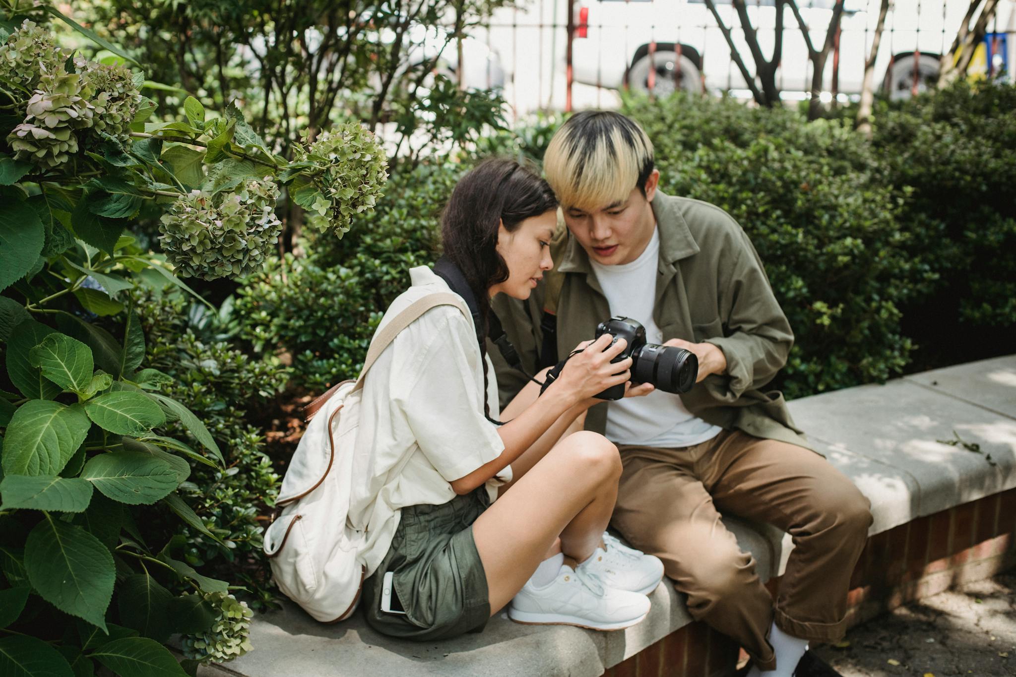 Asian couple using modern photo camera in lush park