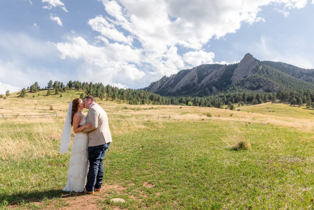 a bride and groom kissing in an open field near flatirons scenery