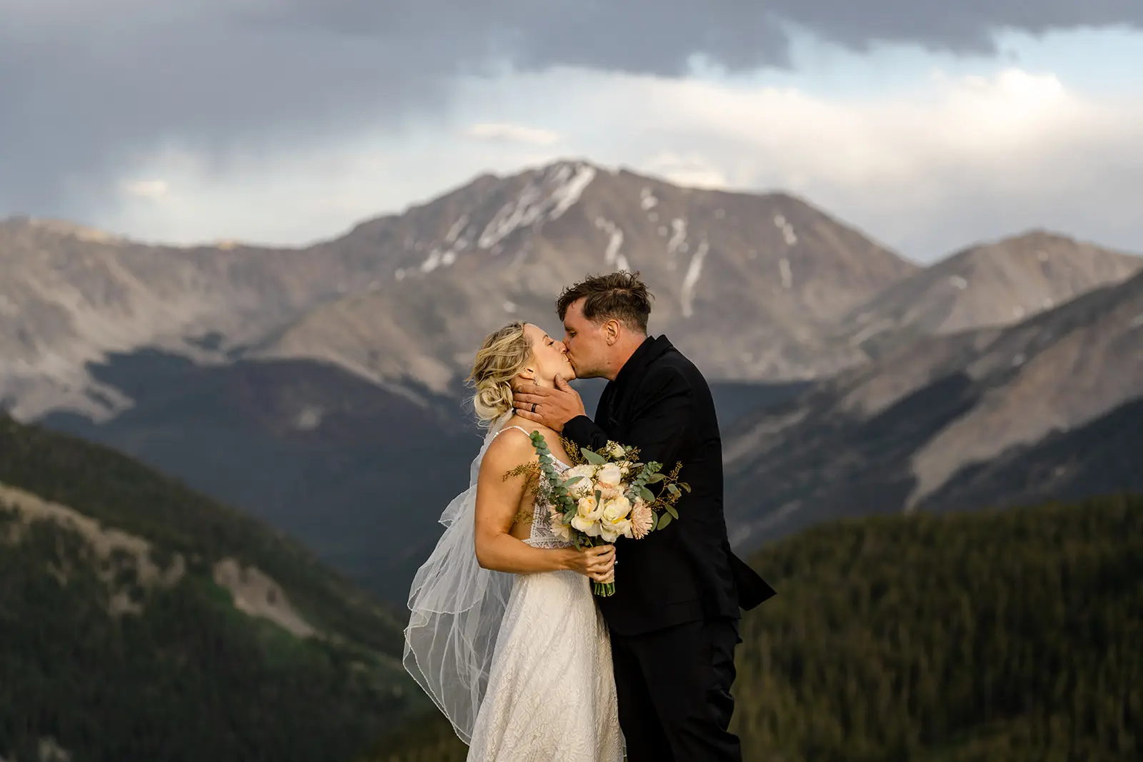 Newlyweds kiss during their outdoor wedding ceremony on a Colorado mountain summit at golden hour