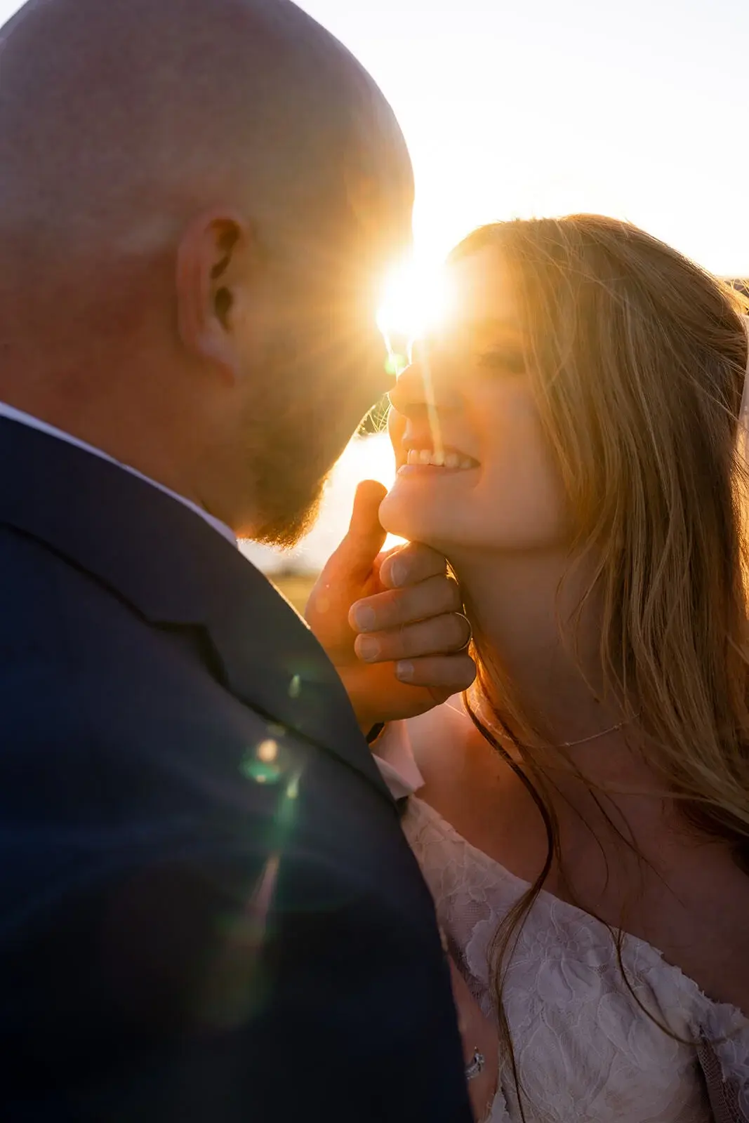 Close-up of a groom gently touching the bride's chin as golden hour sunlight glows between them